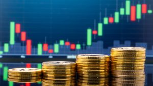 Four stacks of golden coins ascending from left to right with an ascending candle price chart of green and red candles, just above the coins on a dark blue background.