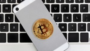 A Bitcoin laying on the back of a cell phone which is on top of a Macbook keyboard