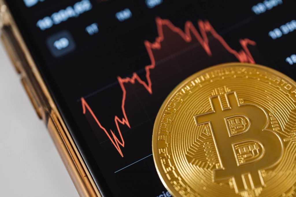 A physical Bitcoin on top of a phone screen with a red price chart line