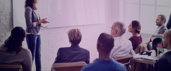 A woman in giving a presentation to a small group of people in front of white board