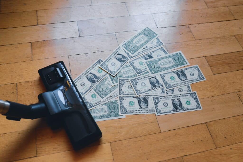 Vacuum sucking up US dollars from a wood floor. Photo courtesy of regularguy.eth at Unsplash