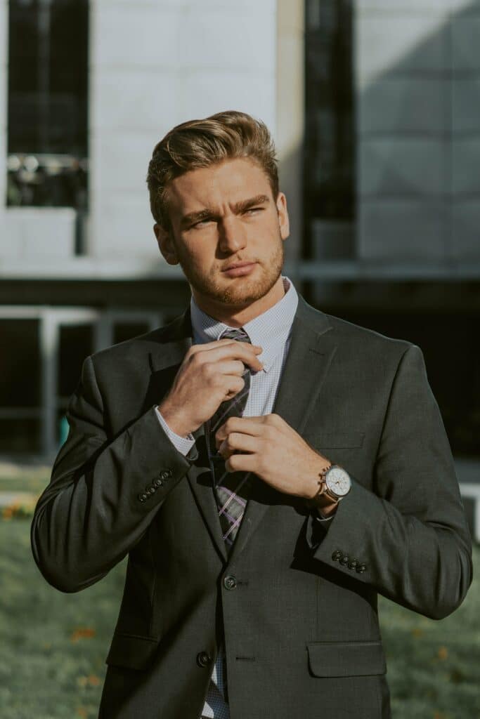 Confident young man in a suit adjusting his tie while looking to the right. Photo by Dinielle De Veyra from Pexels