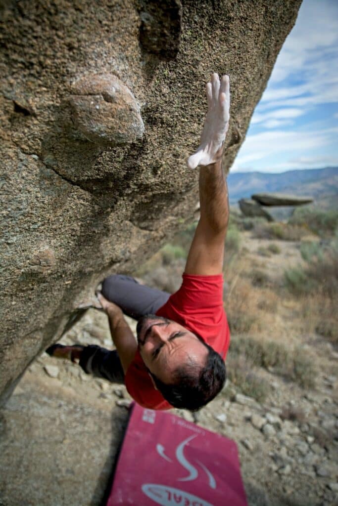 Man free climbing on a rockface reaching for the next hold. Photo courtesy of Rodrigo on Pexels.