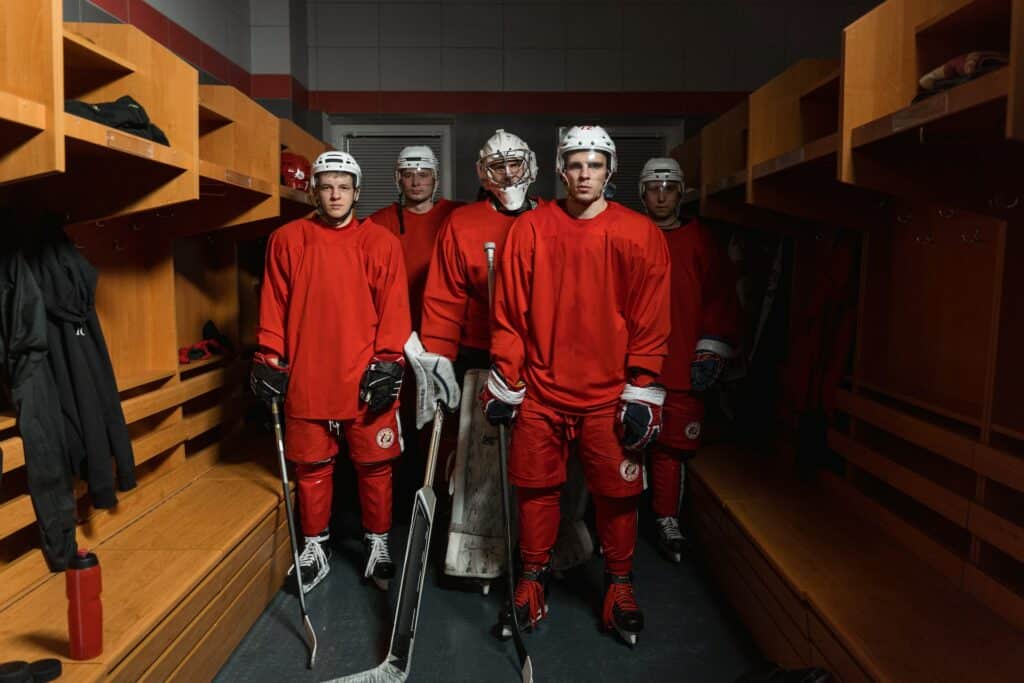 Five somber looking hockey players standing in an empty locker room. Image courtesy of Tima Miroshnichenko at Pexels.
