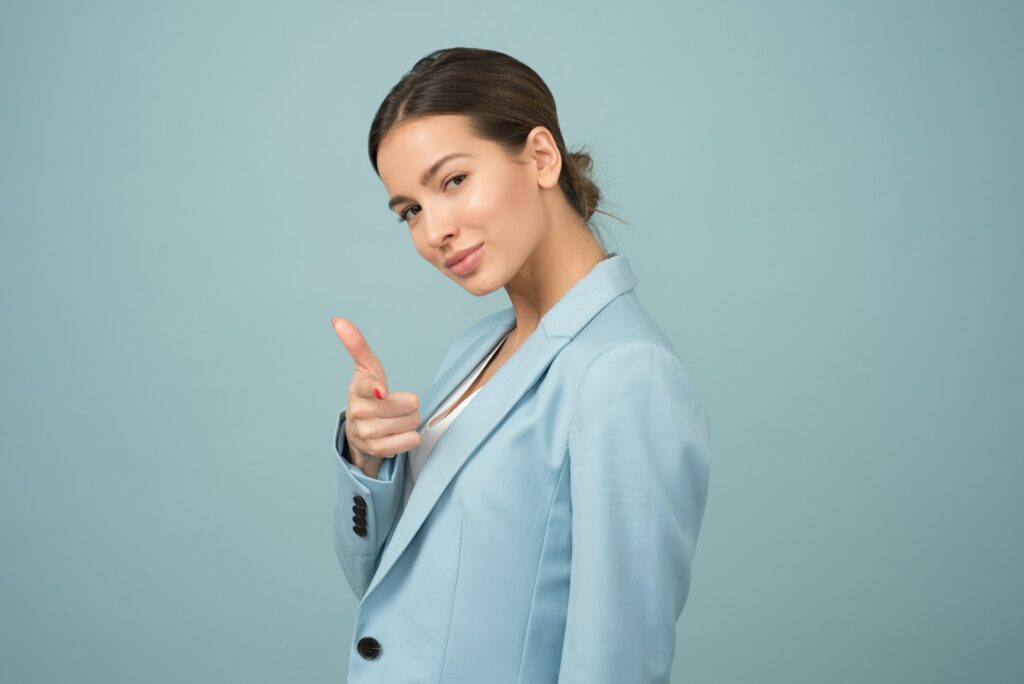 Woman in a suit jacket looking left towards you holding her thumb and index finger like a pistol. Image courtesy of Moose Photos at Pexels. 